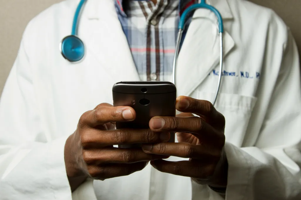 Doctor Holding Cell Phone. Cell phones and other kinds of mobile devices and communications technologies are of increasing importance in the delivery of health care